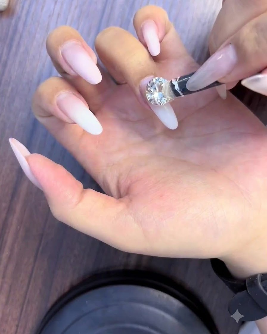 Ein Picker-Werkzeug platziert einen großen, funkelnden Strassstein in der Mitte eines Nagels.