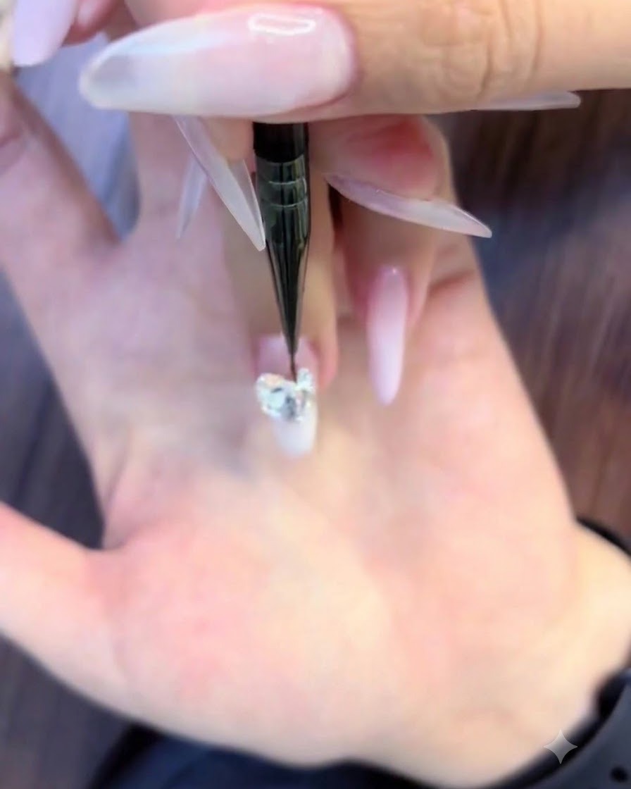 Ein feiner Nail-Art-Pinsel platziert kleine runde Strasssteine um die unteren Ränder eines großen Kristall-Clusters.