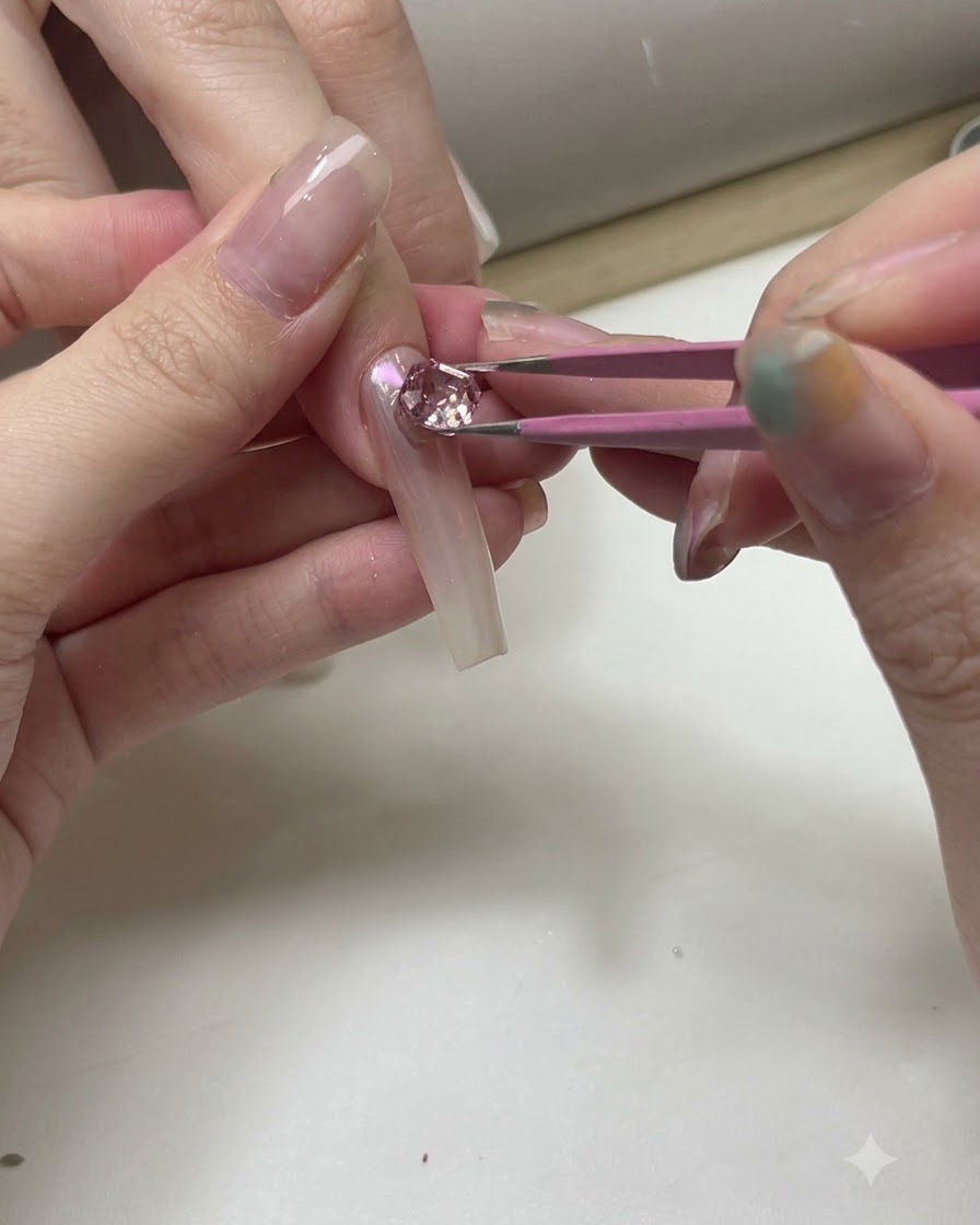 Ein Paar Pinzetten platziert glitzernde rosa und klare Kristalle auf einem transparenten Übungsnageltip.