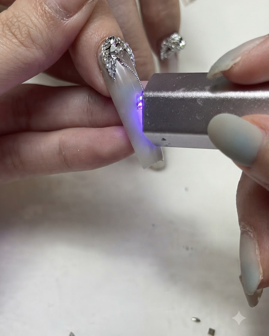 Eine tragbare UV/LED-Taschenlampe härtet feine silberne Gelinien und Strassdetails auf einem dekorierten Nagel aus.