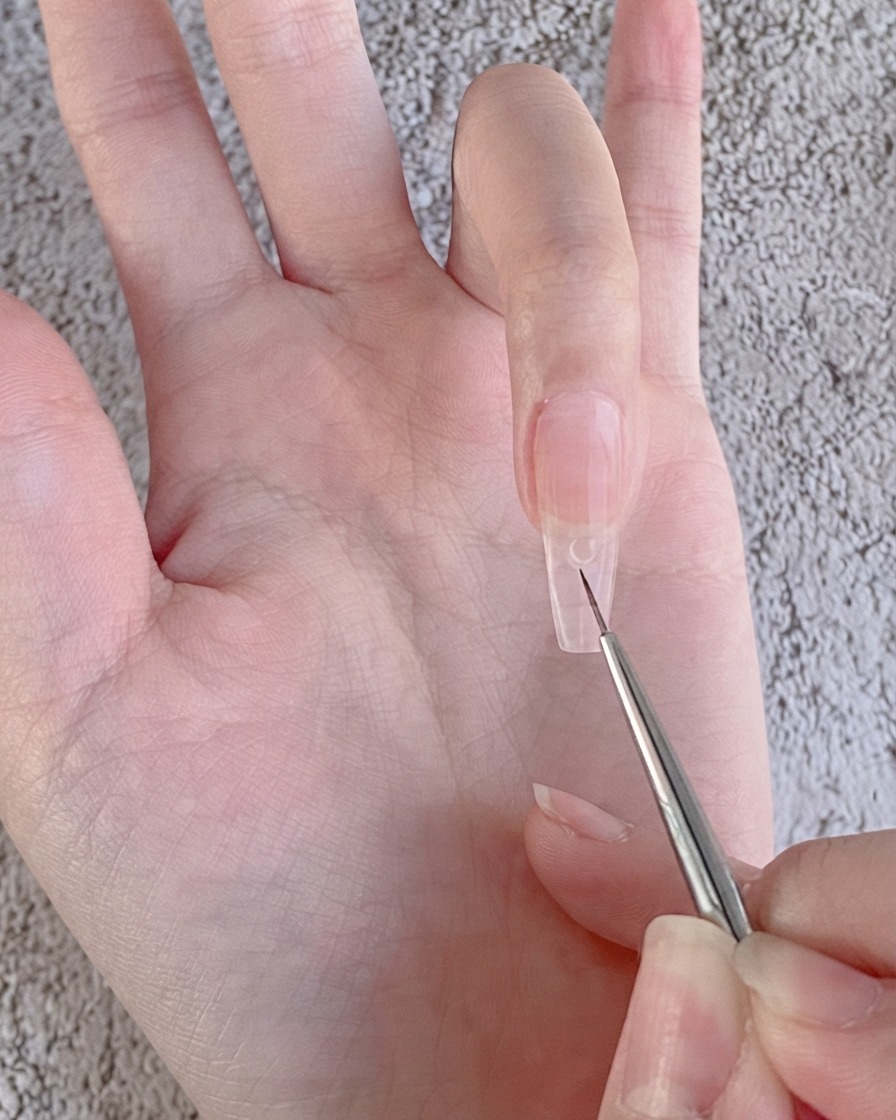 Ein feiner Nail-Art-Liner-Pinsel platziert einen kleinen, klaren Tropfen Strassgel auf einen nude-gelierten Nagel.