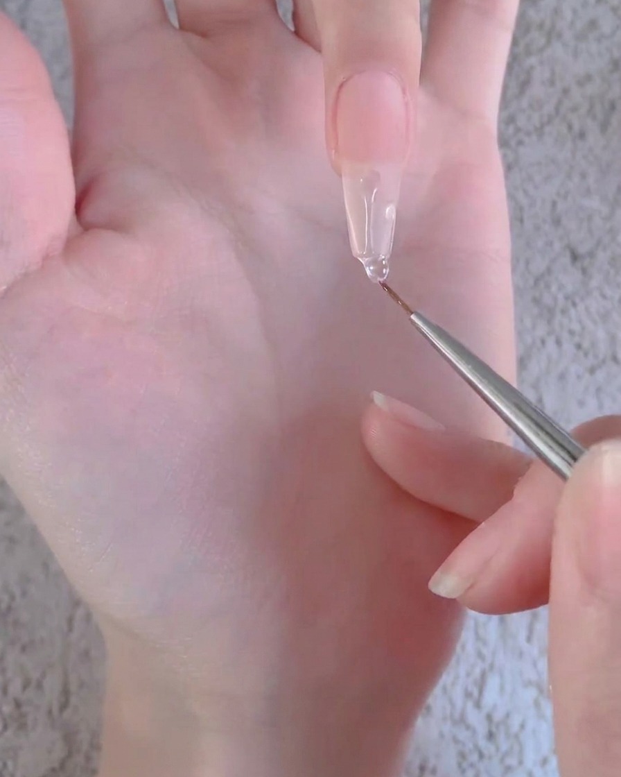 Ein Liner-Pinsel zieht einen klaren Geltropfen nach unten entlang der Länge einer langen künstlichen Nagelverlängerung.