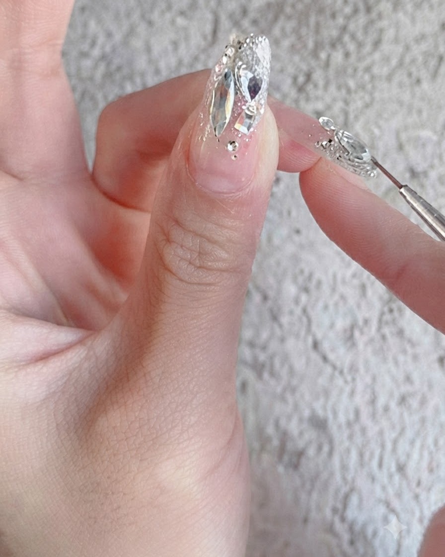 Ein Nagelpinsel trägt einen glänzenden Verstärkungs-Überzug über ein vollständig fertiges Strass-Nageldesign auf.