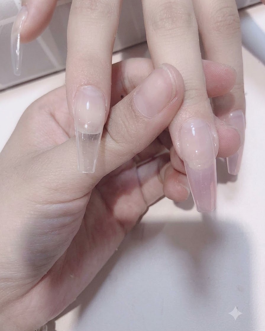 Ein Nagelpinsel verblendet zartes Rosagel nach unten über eine durchsichtige Nagelverlängerung, um einen Verlaufeffekt zu erzielen.