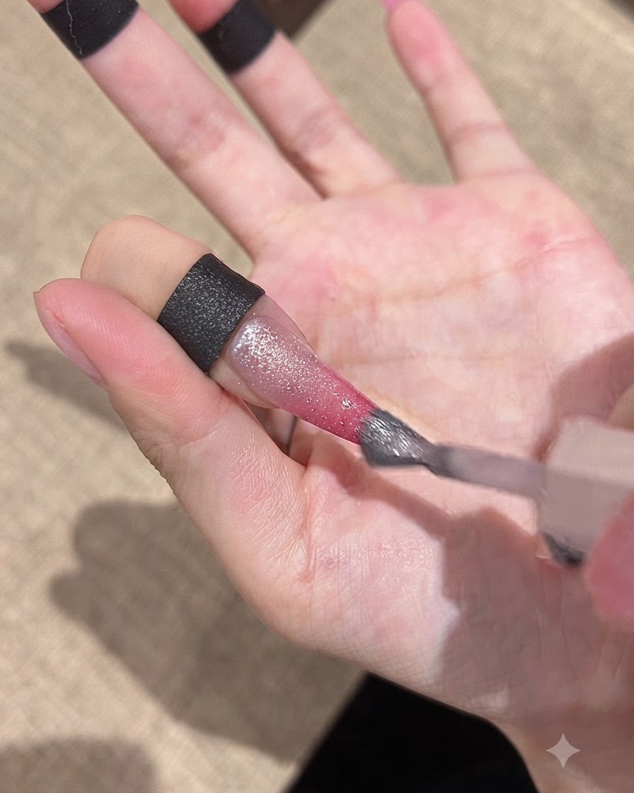 Ein Pinsel trägt ein glitzerndes Cat-Eye-Gel über die Gradient-Nageloberfläche auf.
