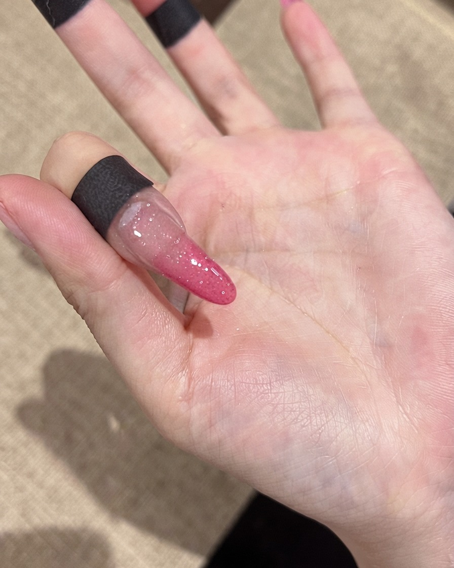 Eine Nahaufnahme eines Nagels zeigt feine reflektierende Glitzerpartikel unter normaler Raumbeleuchtung.