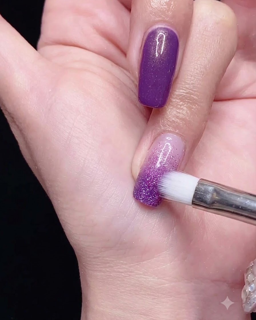 Ein Ombré-Pinsel verblendet lila Gel-Nagellack nach unten über den Nagel für einen sanften Farbverlaufseffekt.