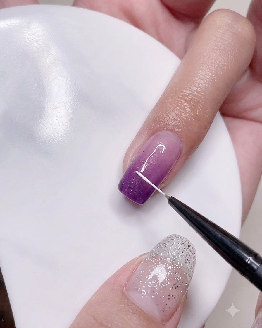 Ein Fine-Liner-Pinsel zeichnet präzise vertikale weiße Linien auf die lila Ombré-Nageloberfläche.