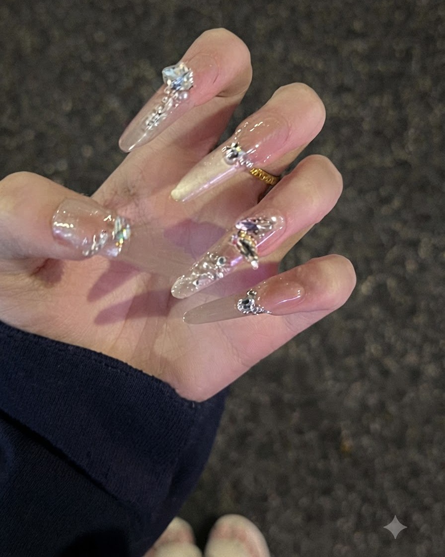 Eine Nahaufnahme einer Hand mit langen Nude Strass-Nägeln, die leicht gekrümmt sind, um das Profil zu zeigen.