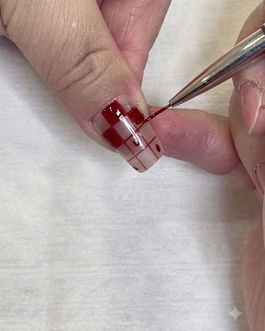 Detaillierte Nahaufnahme, wie ein feiner Nail-Art-Pinsel präzise rotes Gel an den Rand eines Karomusters auf einem Nagel aufträgt.