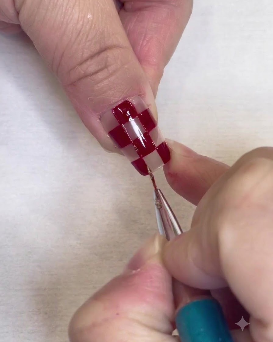 Ein feiner Detailpinsel malt dünne Silberglitter-Ränder entlang der Kanten roter Quadrate auf einem klaren Nagel.