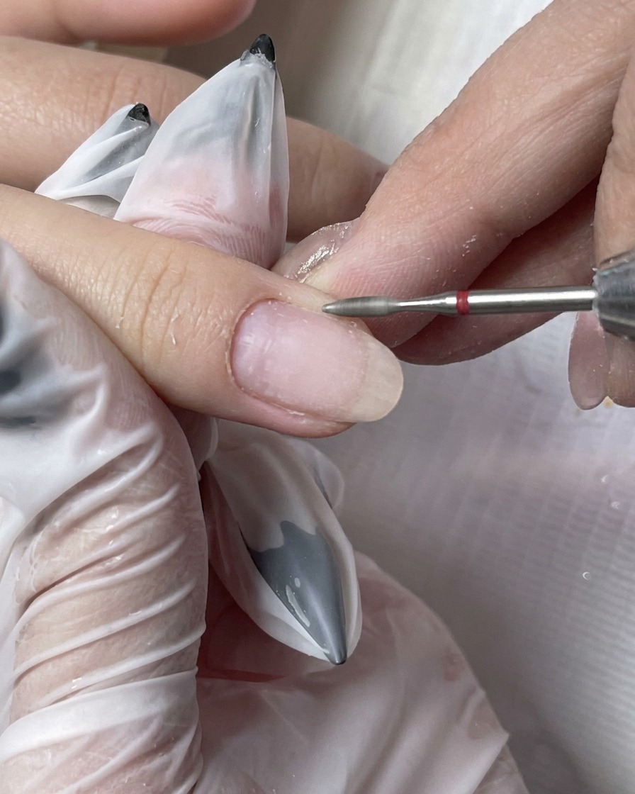 Eine Staubbürste entfernt feine Partikel von einem frisch vorbereiteten Fingernagel.