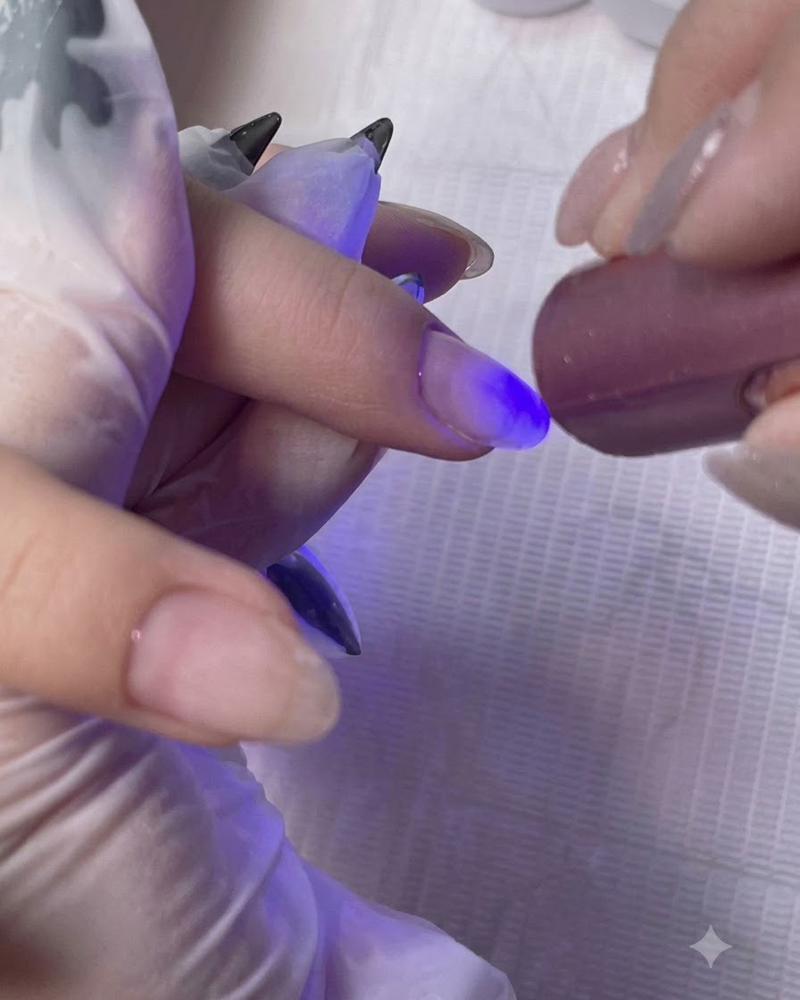 Eine Mini-Hand-UV/LED-Lampe härtet die Base Coat Schicht auf dem Finger einer Kundin aus.