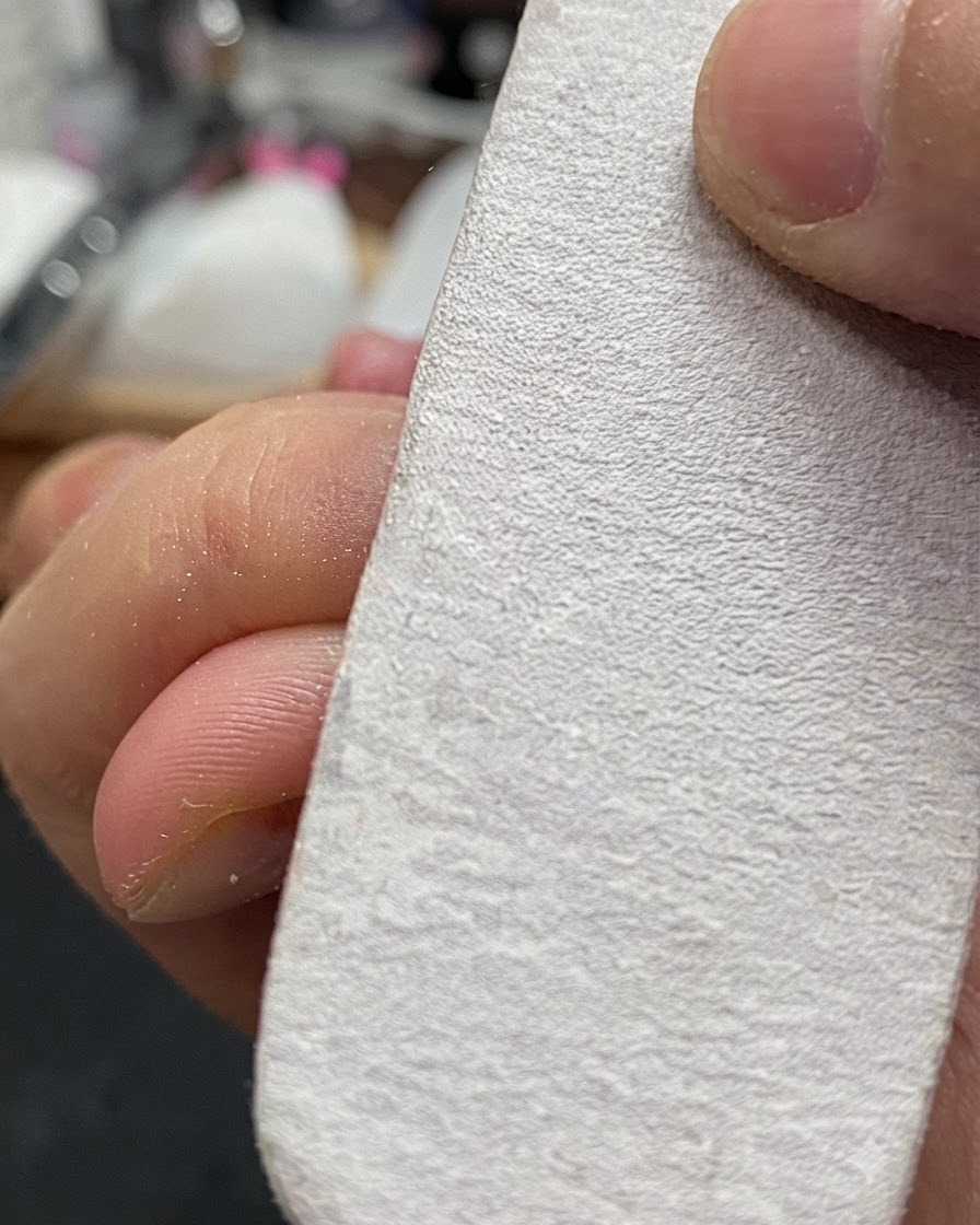 Eine Hand hält einen weißen Nagelpufferblock und feilt leicht die Oberfläche eines Naturnagels.