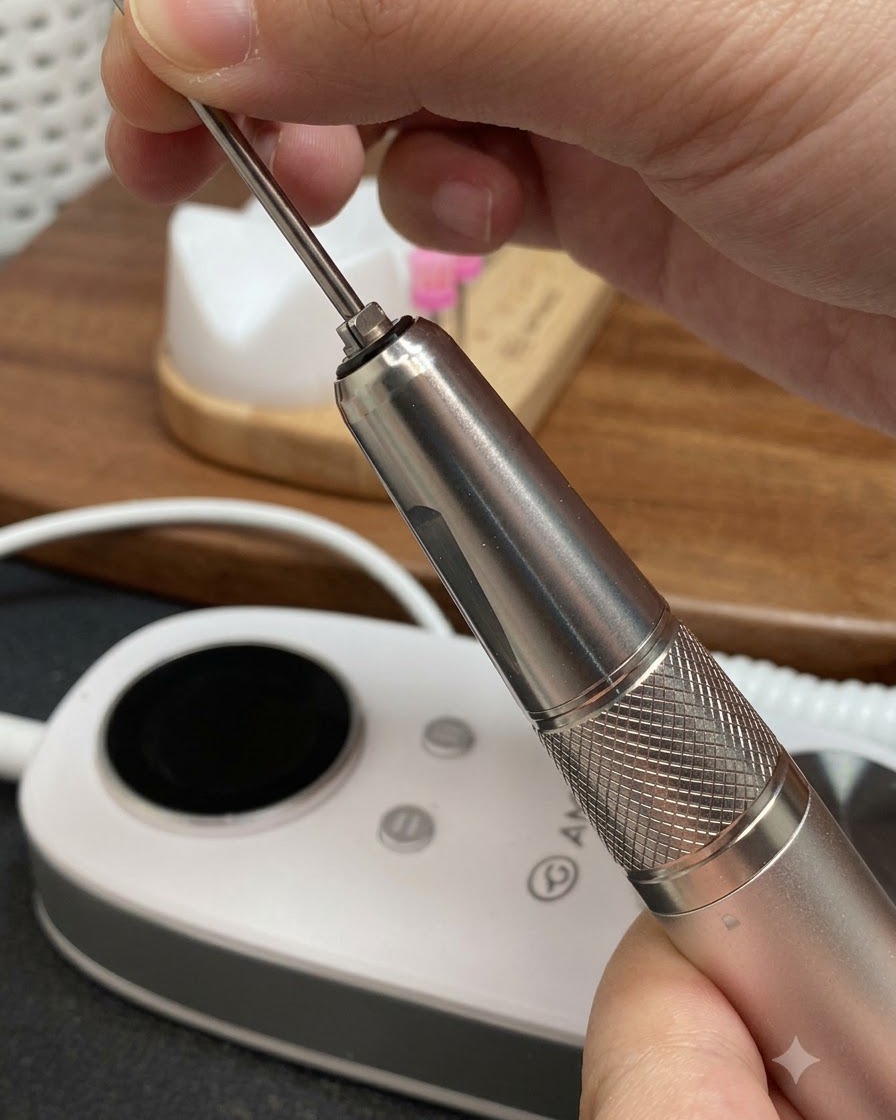Hände setzen einen langen, konischen Metalldräser in das Handstück einer elektrischen Nagelfeile ein.