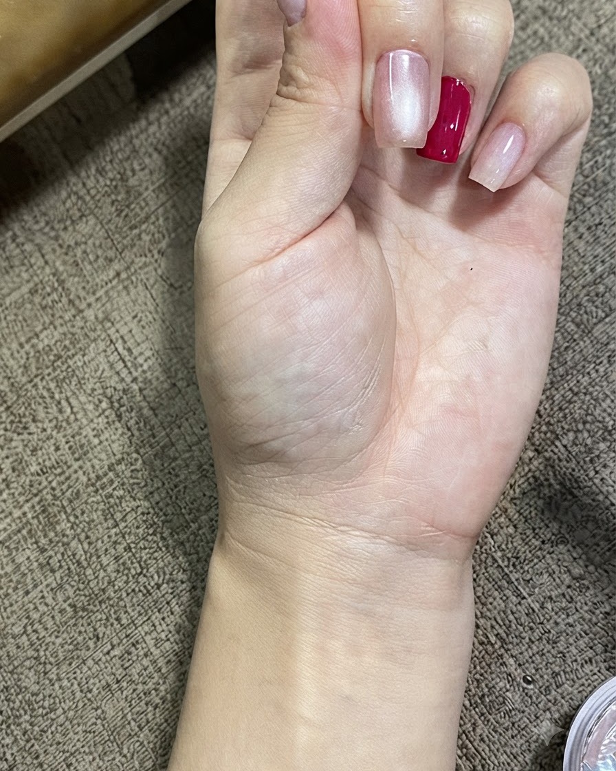 Eine Nahaufnahme einer Hand mit Nägeln, die mit magnetischem Cat-Eye-Gel behandelt wurden, und einen leuchtenden, strahlenden Kugeleffekt zeigt.