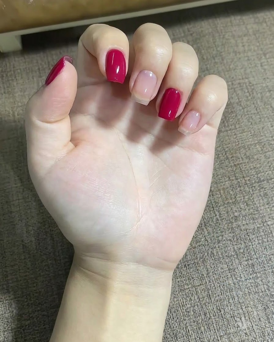 Eine Nahaufnahme einer Hand, die einen feinen Liner-Pinsel verwendet, um kleine rote Punkte nahe einem Sterndesign auf dem Mittelfingernagel aufzutragen.