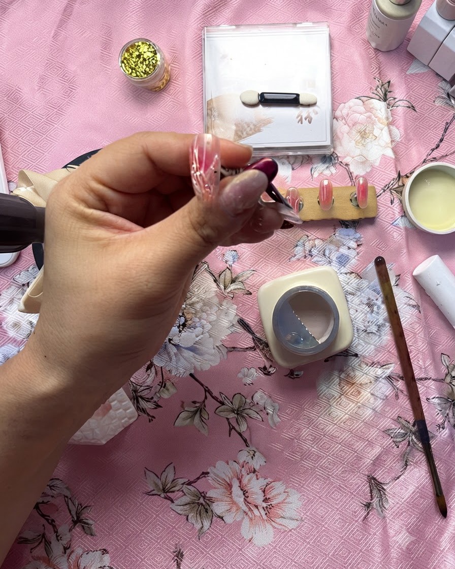 Nahaufnahme einer Nageldesignerin, die mit einem feinen Pinsel eine erhabene klare Gellinie über einem weißen Herzdesign zieht.