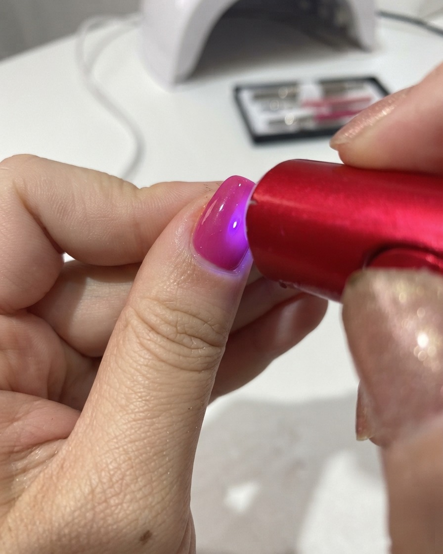 Eine tragbare rote UV-/LED-Lampe härtet das Gel-Polish auf einem Fingernagel aus.