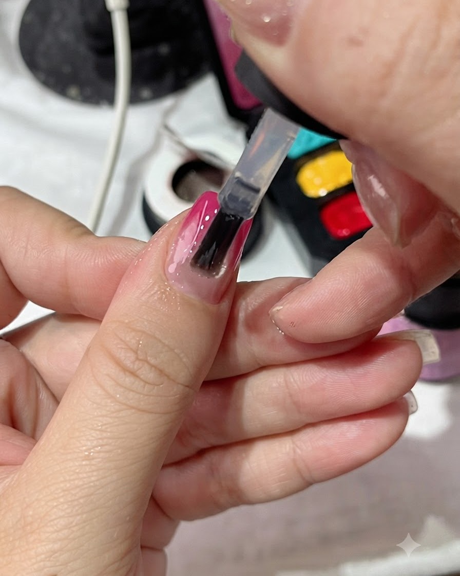 Ein Lackierpinsel trägt einen klaren Topcoat gleichmäßig über einen nageldesignierten Farbverlaufsnagel auf.