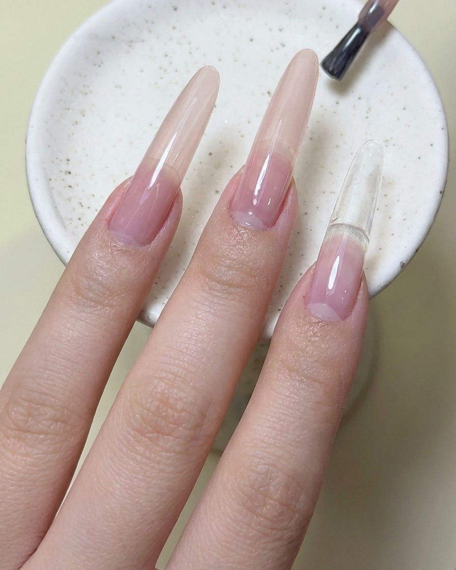 Ein Nagelpinsel trägt magentaroten Gel-Nagellack auf den Zeigefingernagel auf.
