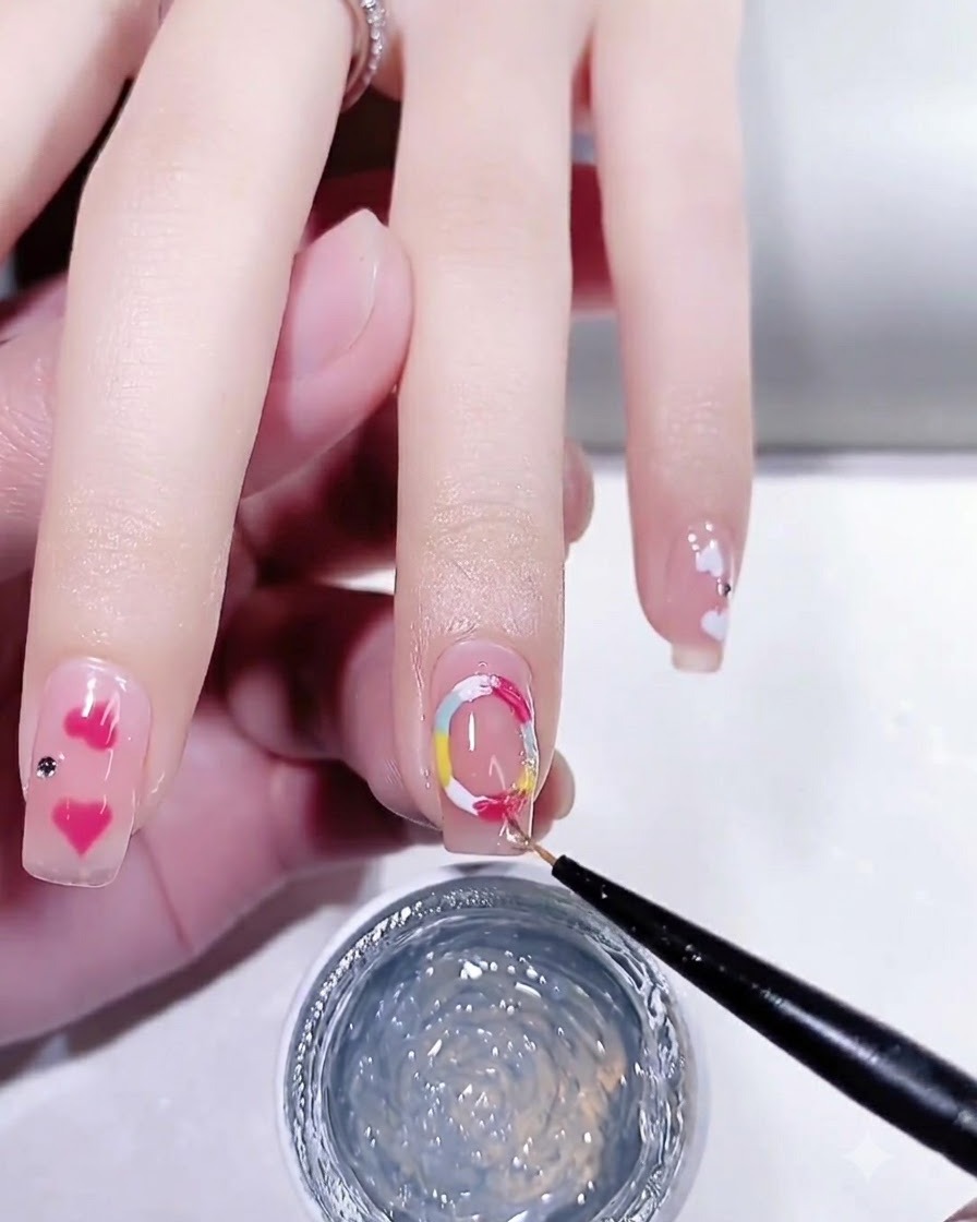 Ein feiner Nail-Art-Pinsel trägt einen glänzenden Überlack über einen gepflegten Nagel mit bunten Punkt-Details auf.