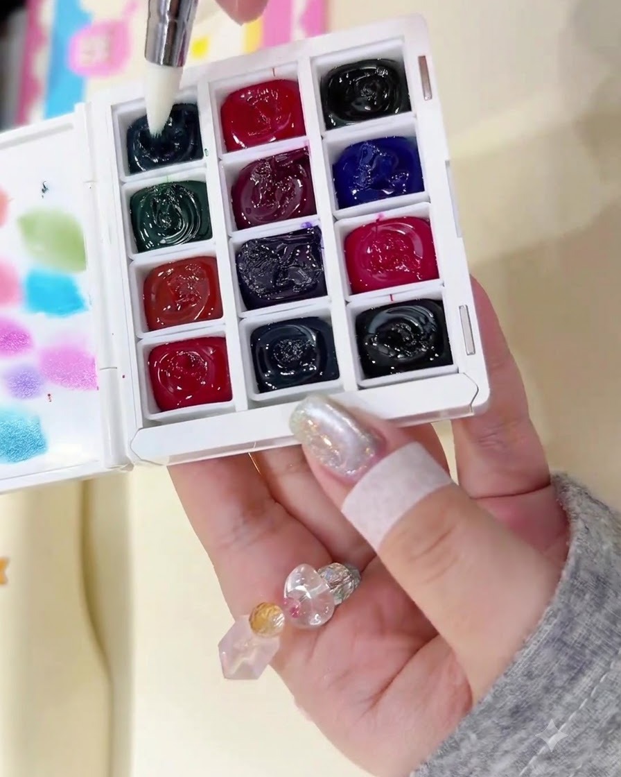 Ein feiner Pinsel wird in ein dunkles Tintenfass auf einer Aquarellpalette getaucht.