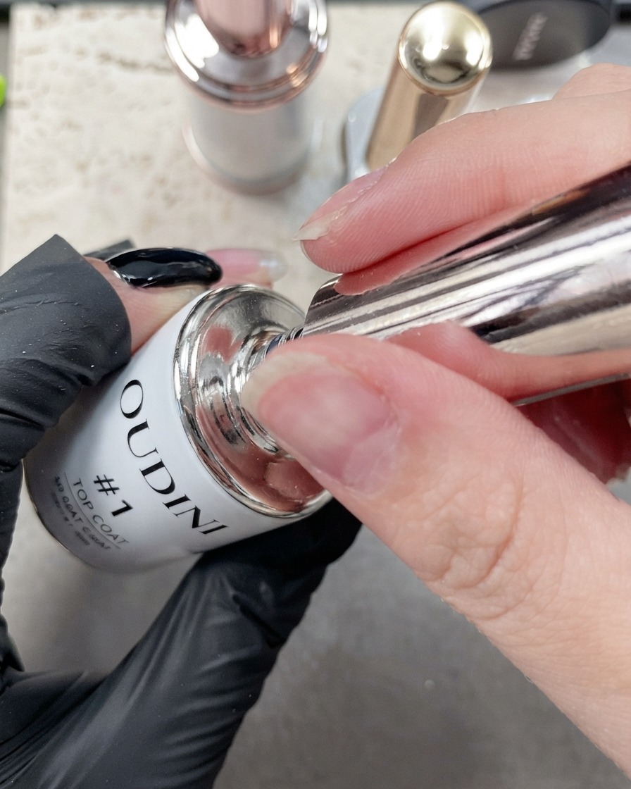 Nahaufnahme eines feinen Pinsels, der Top Coat entlang der Kante eines manikürten Zeigefingernagels aufträgt.