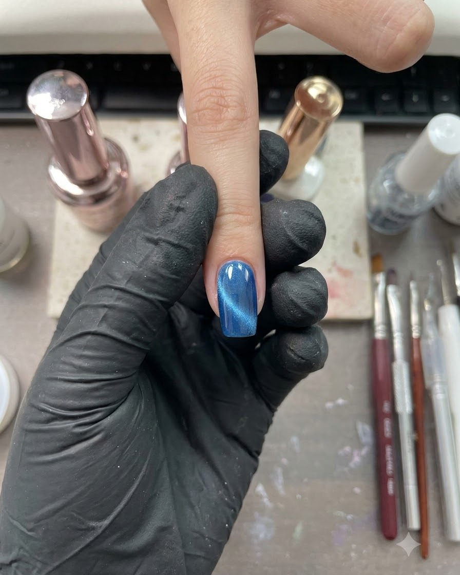 Ein einzelner Finger mit glänzendem blauem Cat-Eye-Finish unter einer Nagelstudiolampe positioniert.