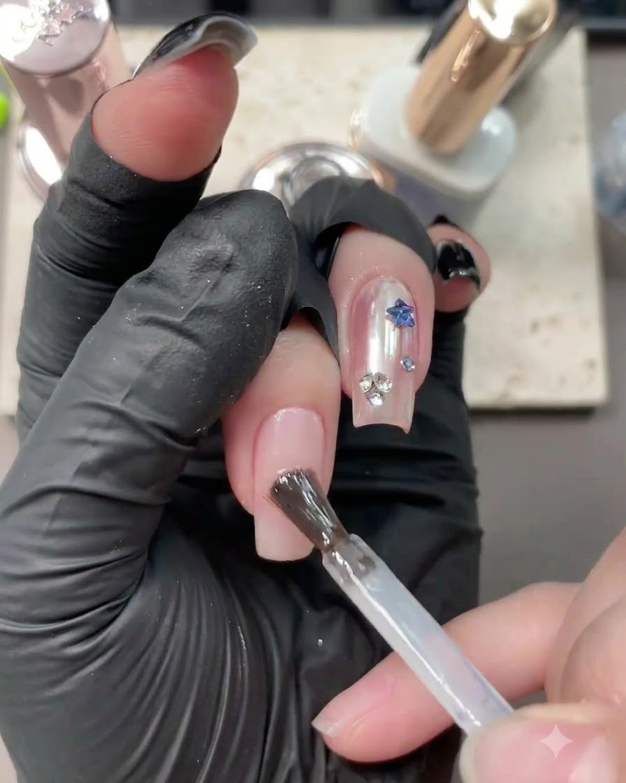 Ein Pinsel trägt klares Basisgel auf einen neutralen Nudenagel mit bestehendem Nail Art auf.