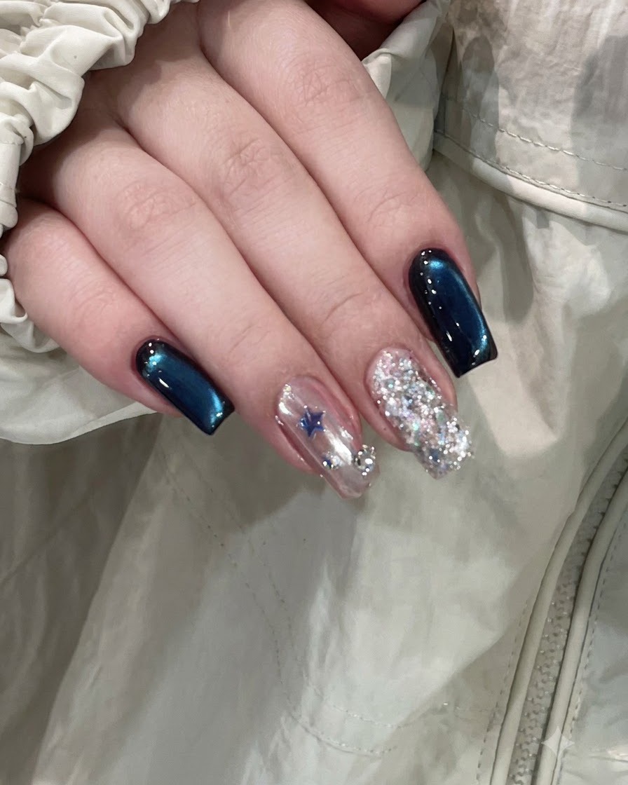 Eine fertige Hand zeigt tiefblaue Cat-Eye-Nägel neben einem sternverzierten Akzentnagel und einem vollen Glitzernagel.