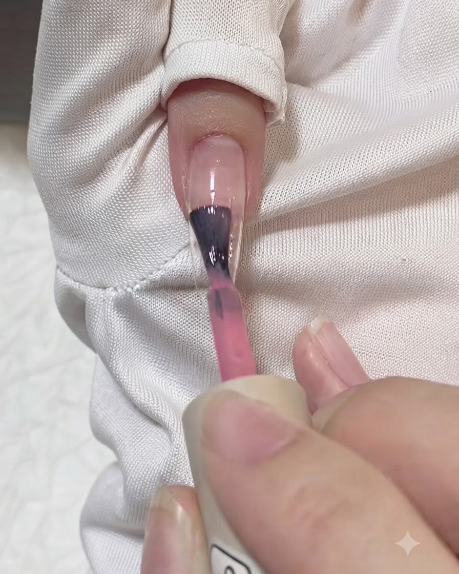 Ein Pinsel trägt einen Strich durchscheinendes Rosagel in der Mitte einer klaren Nagelverlängerung auf.
