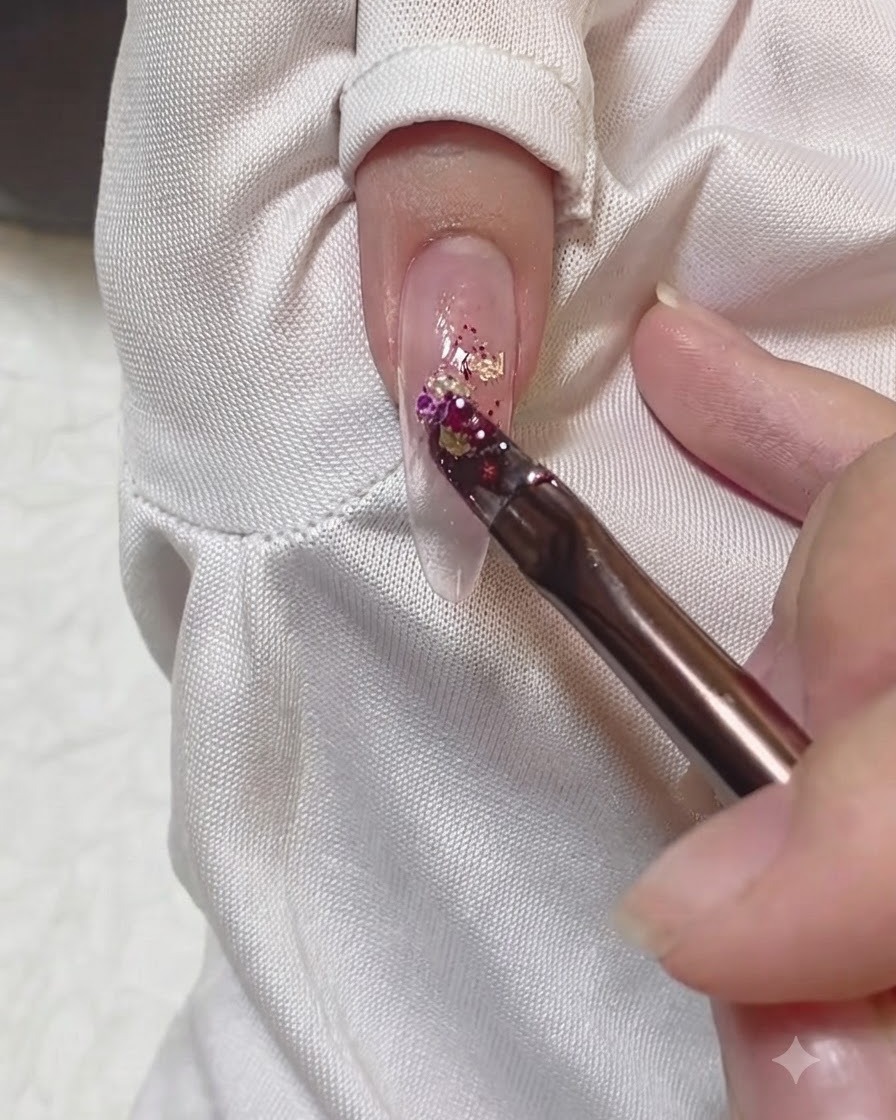Ein Pinsel trägt eine Ansammlung bunter Glitzerflocken in die Mitte eines Nagels auf.