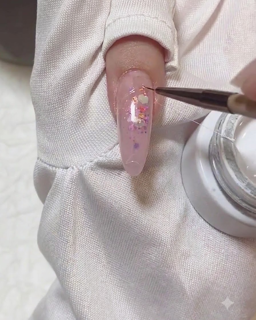 Ein Detailpinsel zieht einen feinen Strang weißen Spider-Gels über einen manikürten Nagel.