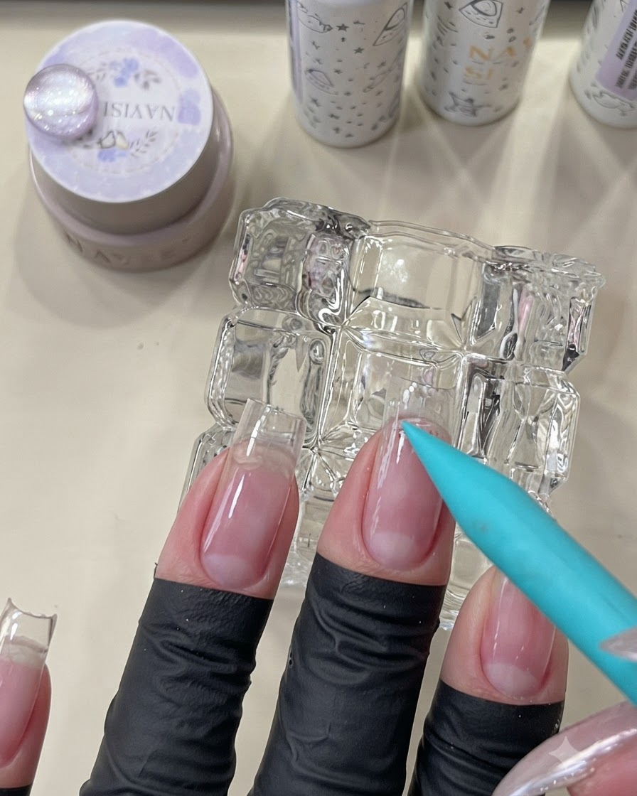 Ein blauer Pinsel trägt einen klaren Peel-Off-Unterlack auf den Nagelutikelbereich eines Naturnagels auf.