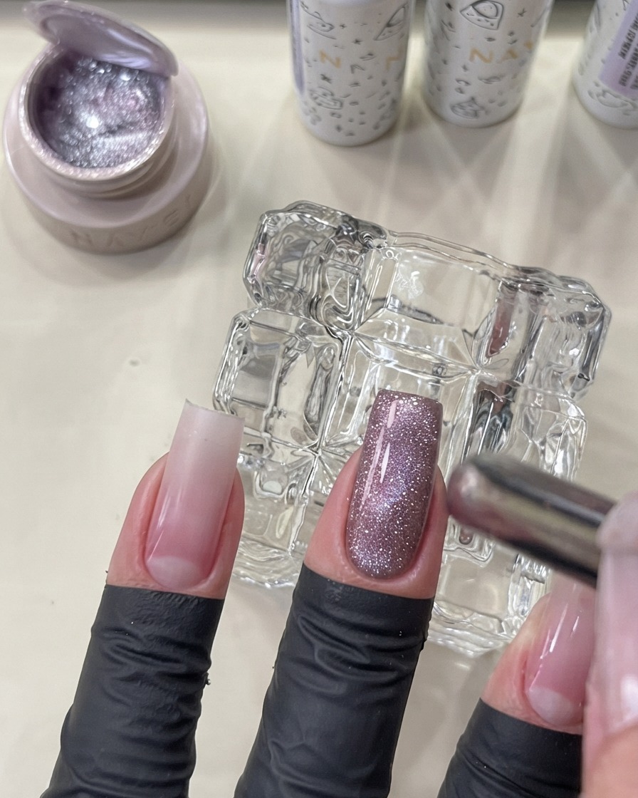 Ein Magnetwerkzeug wird nahe an einen manikürten Nagel gehalten, um das Flashing Cat-Eye-Gel in einen leuchtenden Glaseffekt zu formen.