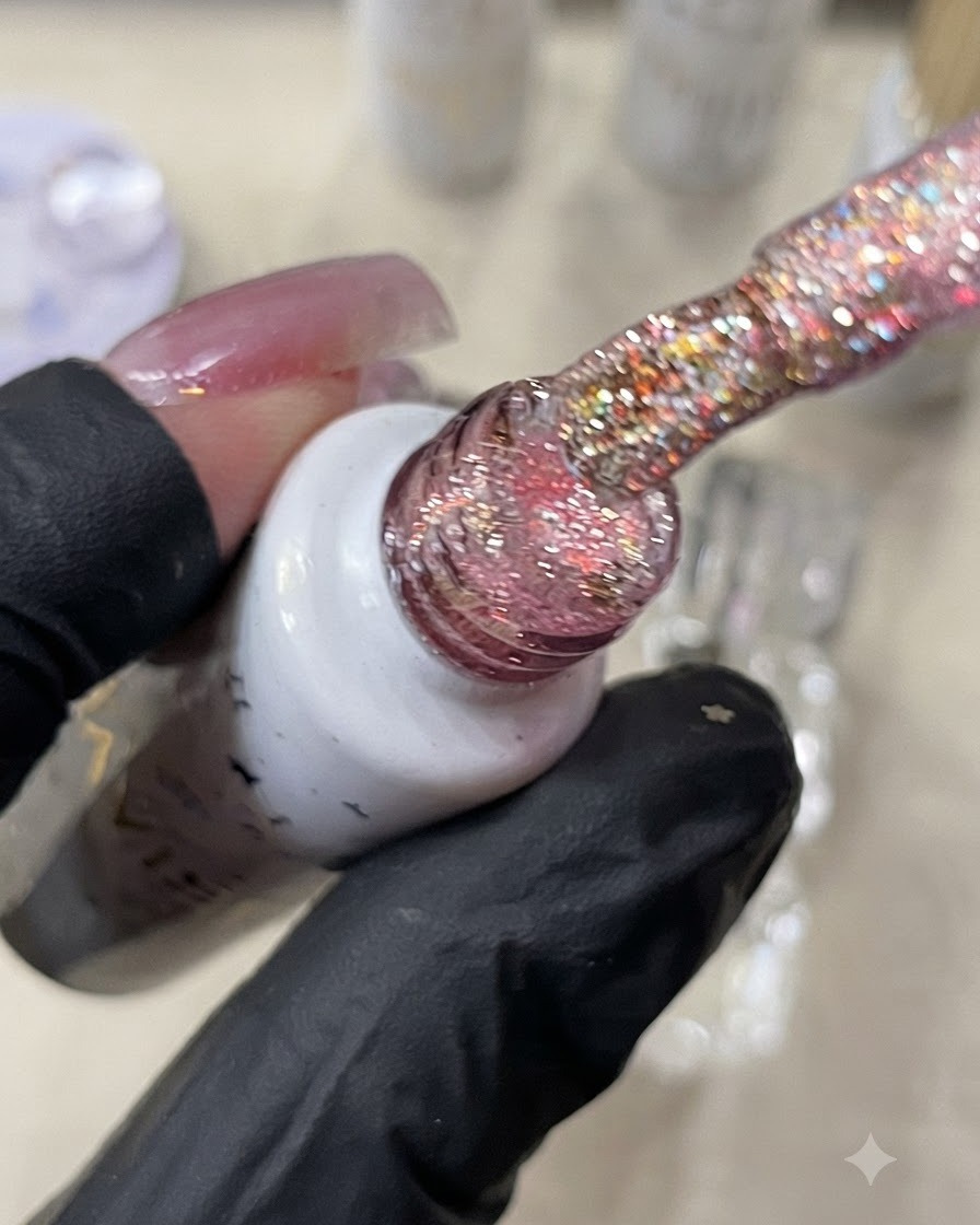 Ein Pinsel hält warmes Orangeglitter-Gel über einen Nagel.