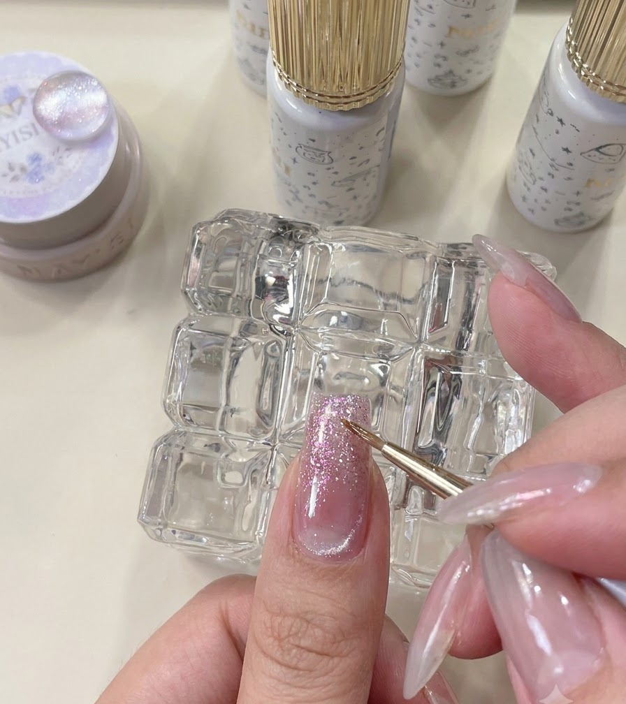 Ein feiner Liner-Pinsel verblendet einen Orangeglitter-Akzent auf einem manikürten Nagel.