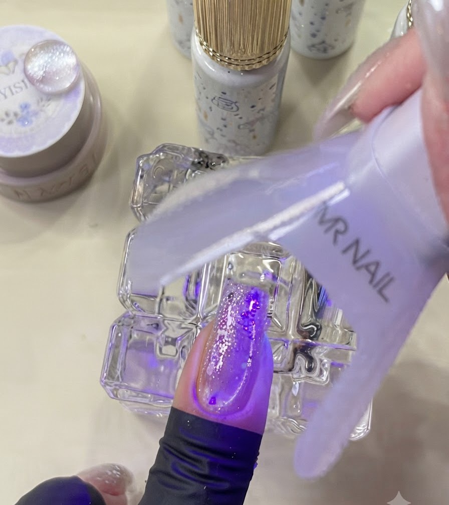 Eine Mini-UV-Lampe härtet einen verzierten Nagel unter violettem Licht aus.