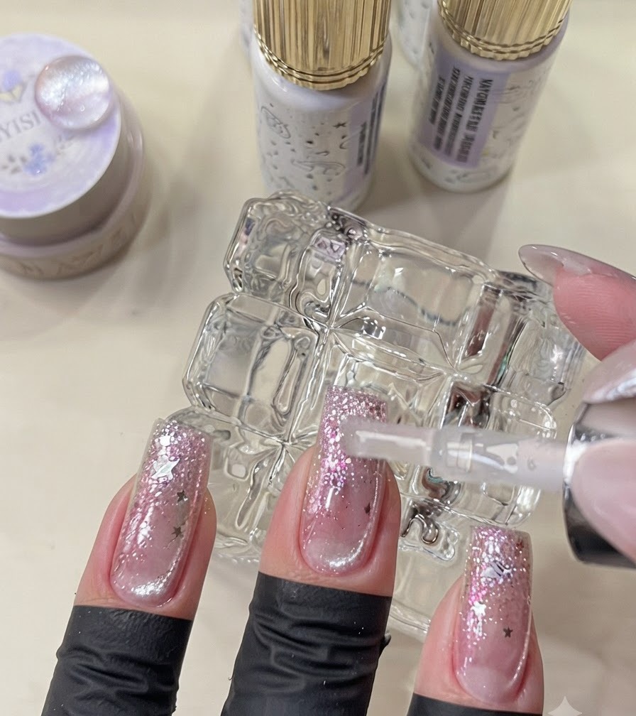 Ein Pinsel trägt den finalen Topcoat auf fertige Galaxy-Style-Nägel auf.