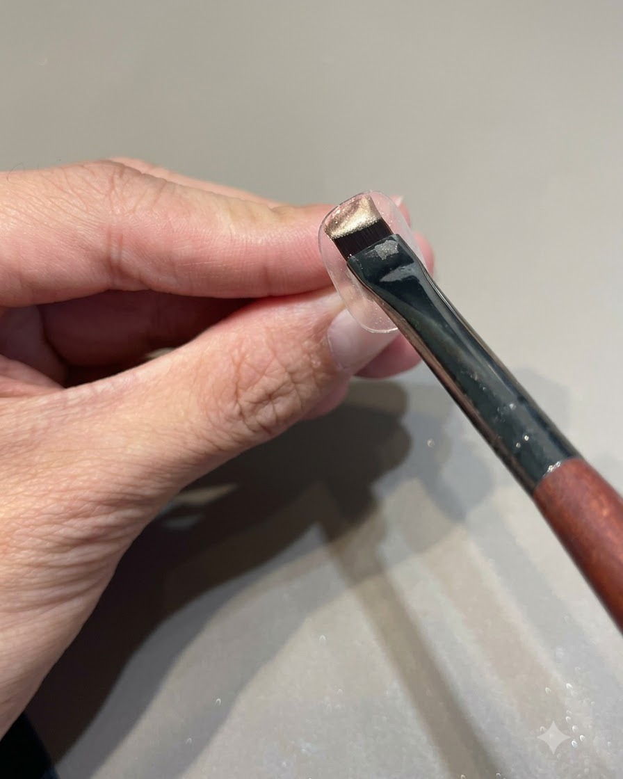 Ein Pinsel mit pinkgoldenem Cat-Eye-Gelack wird über einen klaren Nagel-Display-Ständer gehalten.