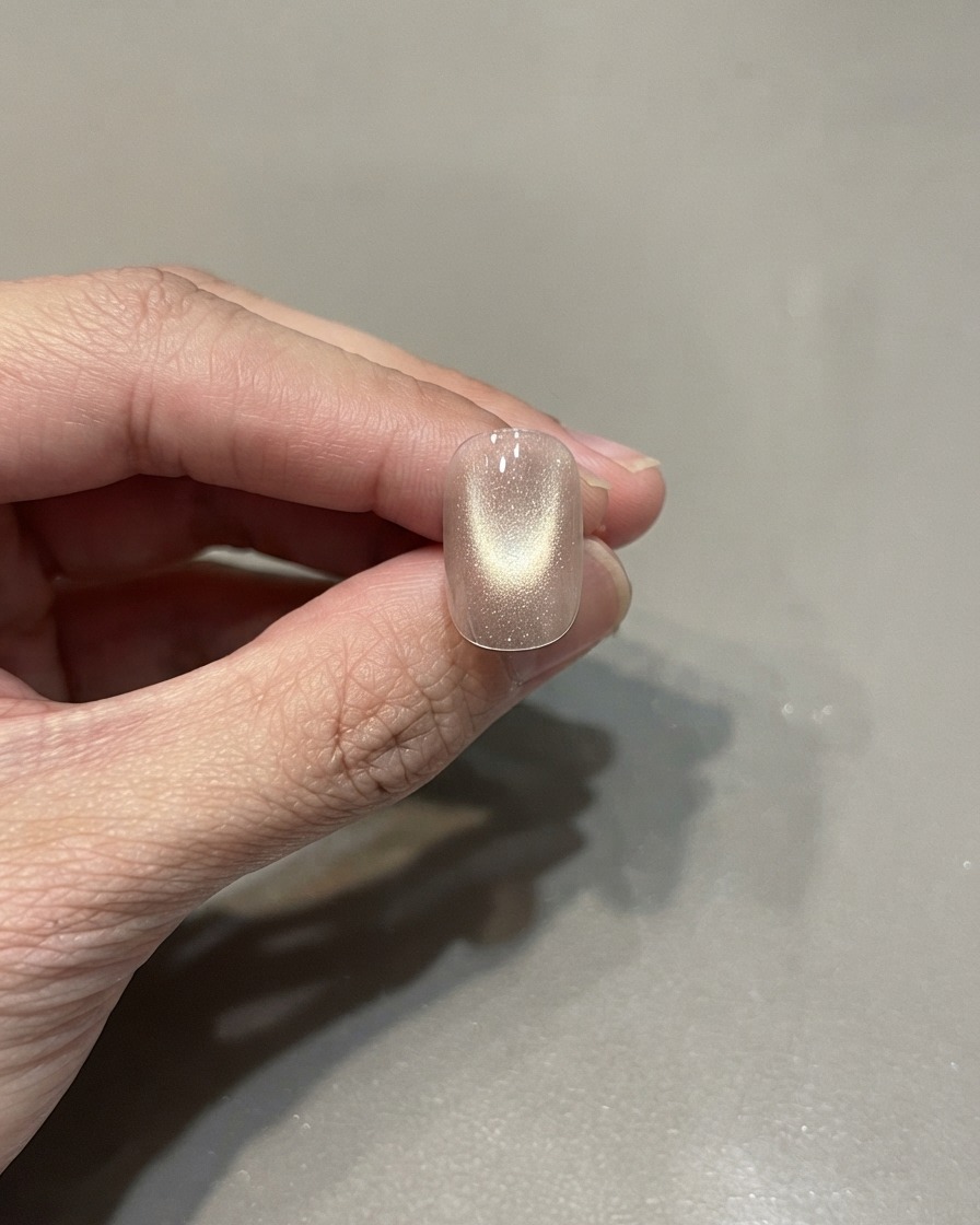 Ein einzelner manikürter Nagel mit ausgehärtetem pinkgoldenem Cat-Eye-Lack und zentrierter Lichtreflektion.