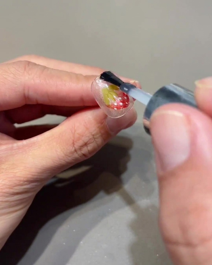 Ein Pinsel trägt einen klaren Topcoat über einen dekorierten Nagel auf.