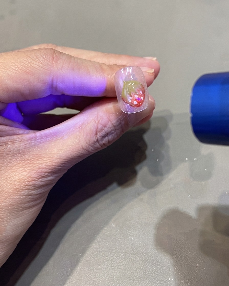 Eine tragbare UV-Taschenlampe härtet ein 3D-Erdbeer-Nageldesign aus.