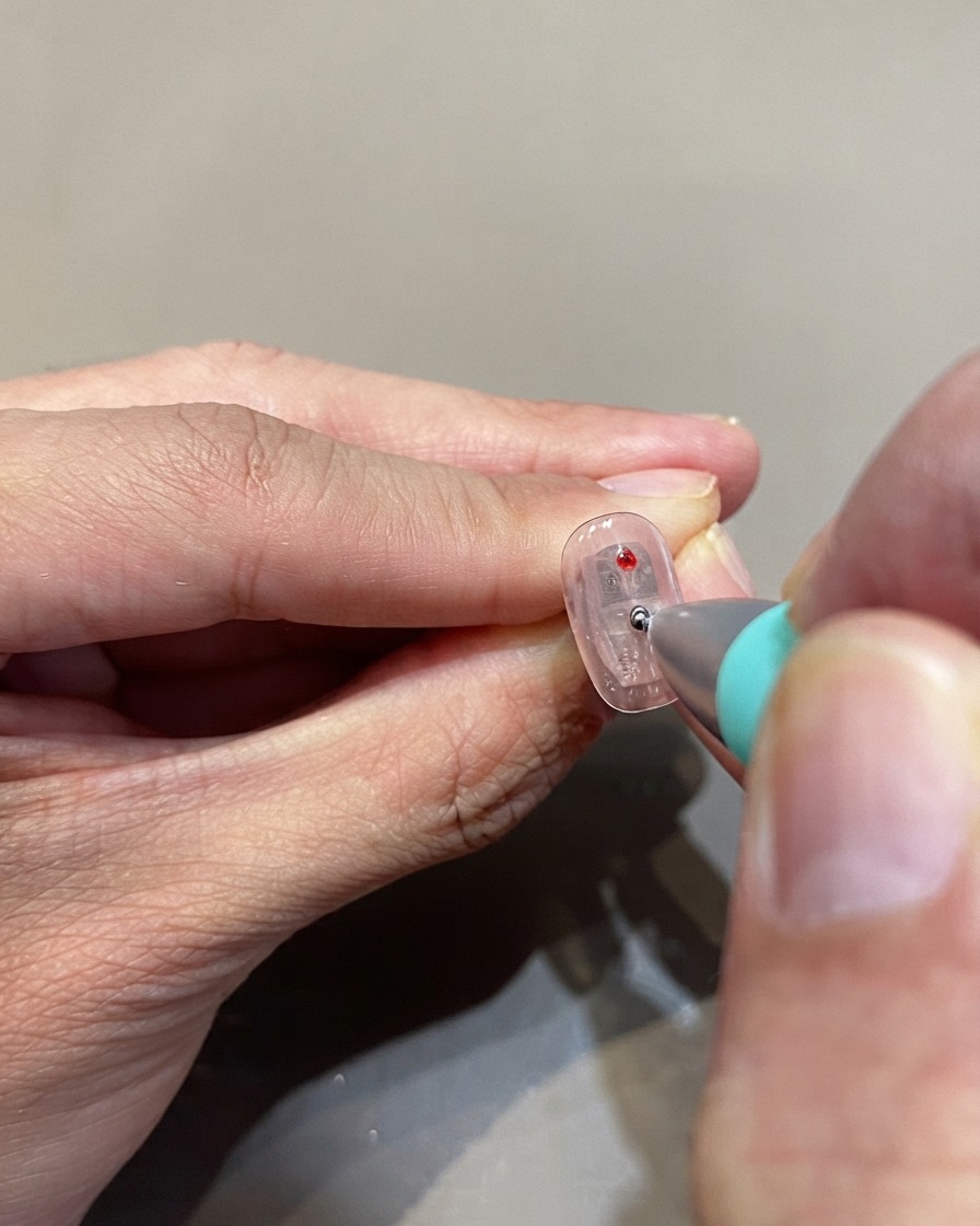 Ein Dotting-Tool platziert rote Glasgel-Polka-Dots auf einer klaren Nageloberfläche.
