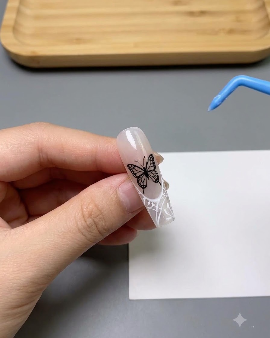 Nahaufnahme eines Nagels, der mit einem detaillierten, weißen und filigranen Schmetterlingsmuster verziert ist.