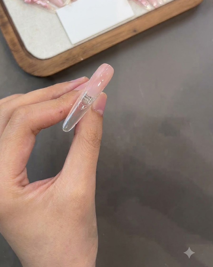 Eine Hand hält einen Nagel kopfüber, während Base Gel auf die Rückseite aufgetragen wird.