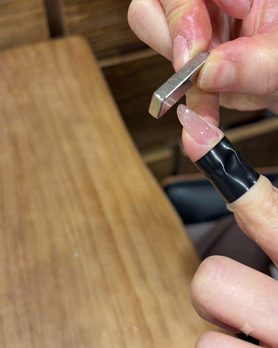 Ein rechteckiger Stabmagnet, der senkrecht in der Nähe eines glänzend gelackten Fingernagels gehalten wird, um die magnetischen Partikel zu verschieben.