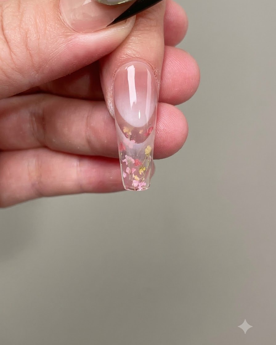 Eine Pinzette platziert winzige rosa und gelbe Trockenblumen auf dem feuchten Nagelgel.