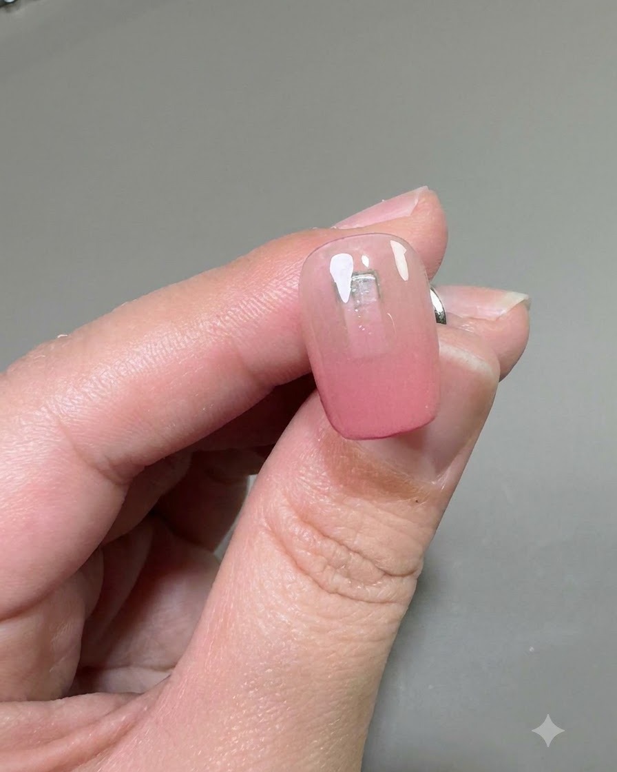 Nahaufnahme eines Nagels mit einer klaren Schicht Verstärkungsgel über der rosa Ombré-Basis.